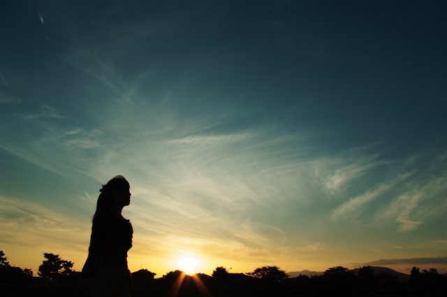自分はいらない人間と落ち込んで夕日を眺めている女性のシルエットの画像