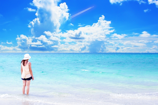 海辺で立っている白い帽子をかぶった女性の画像