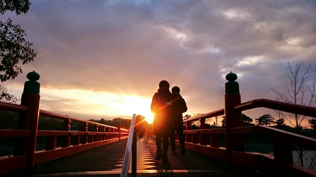 夕焼けに染まる橋で二人のカップルが立っている画像