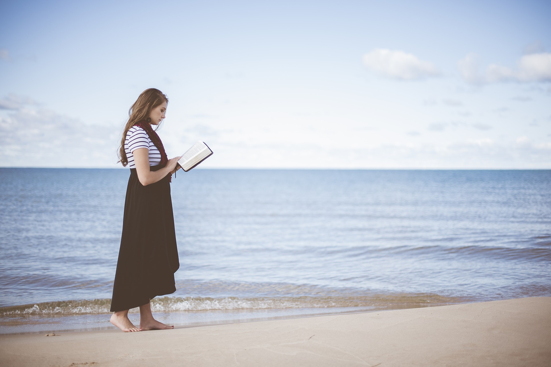自己啓発本を海岸で歩きながら読んでいる女性の画像