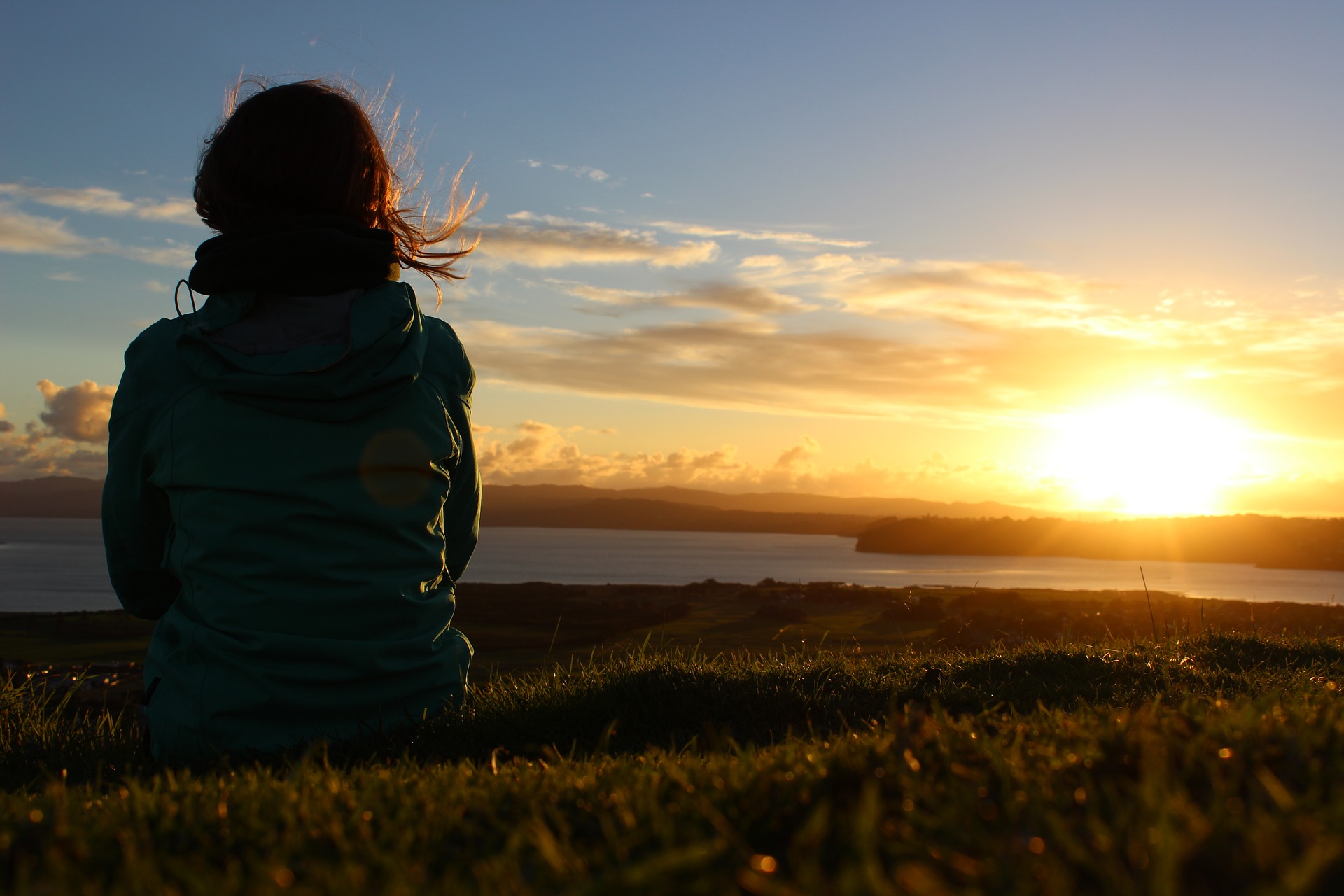 セラピストの仕事に悩んでいる女性が夕日を見つめている後ろ姿の画像