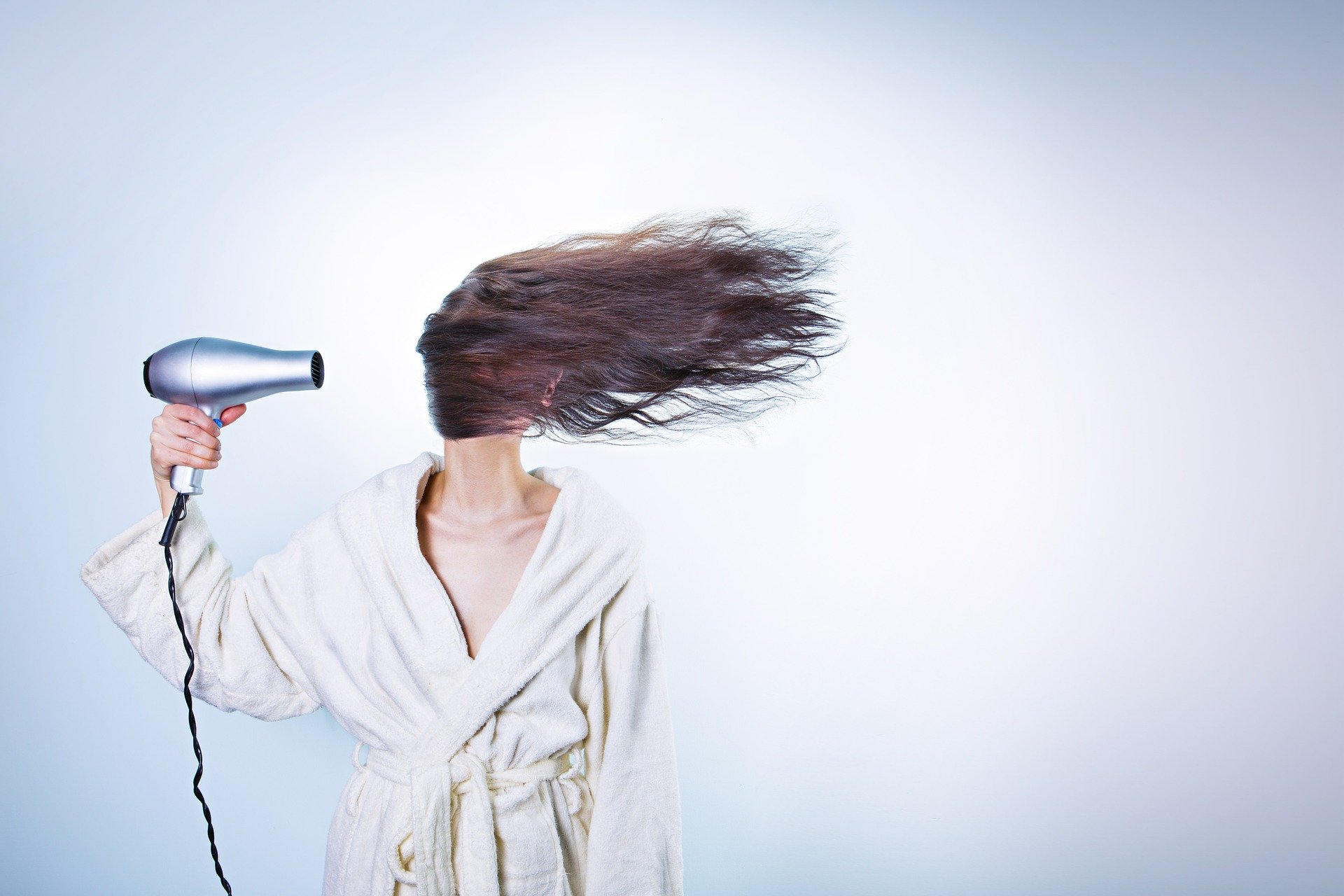 髪の毛をバッサリ切るか悩んでいる長い髪をドライヤーで乾かしている女性の画像