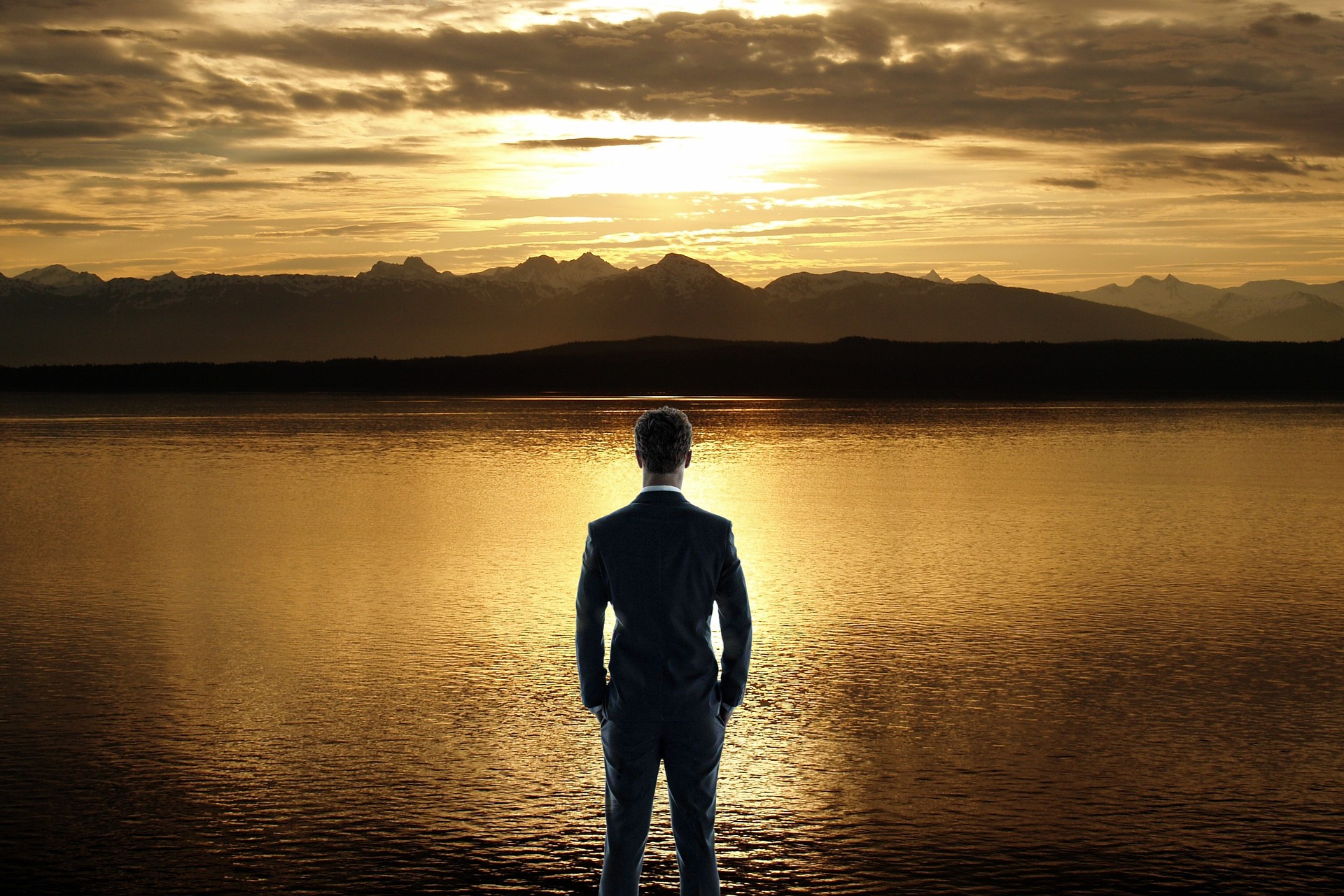 一流と呼ばれるビジネスマンが夕焼けの湖を見ている画像