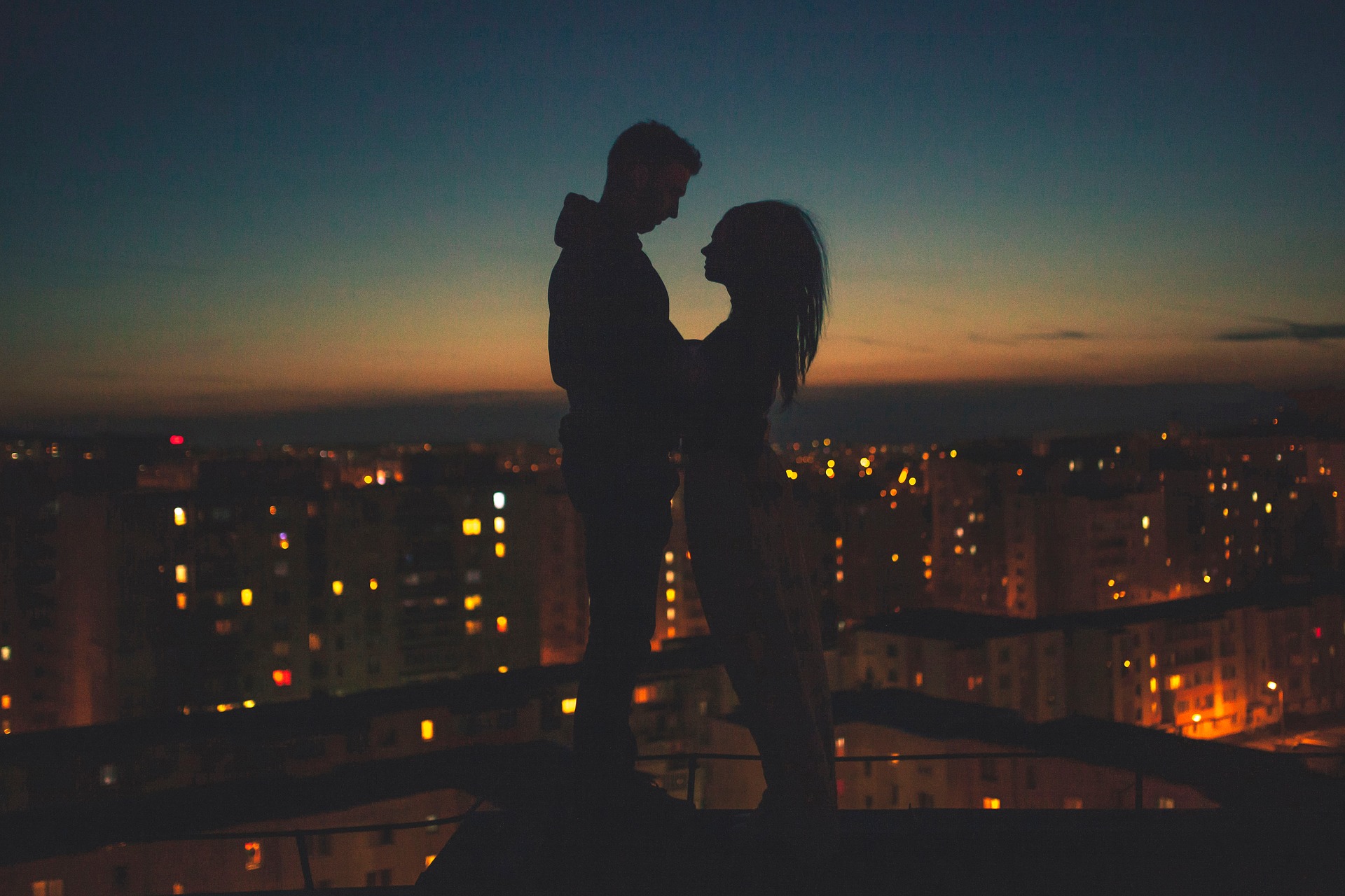 夜の屋上で見つめ合うツインレイカップルのシルエットの画像