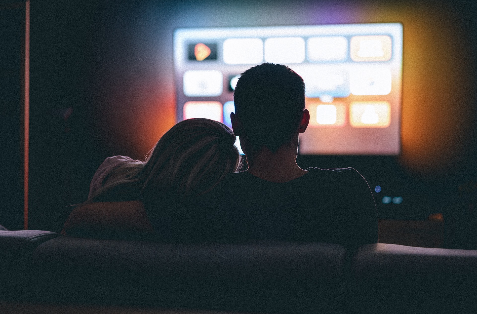 嫉妬深いツインレイ男性がツインレイ女性の肩に腕をまわしてテレビを見ている画像