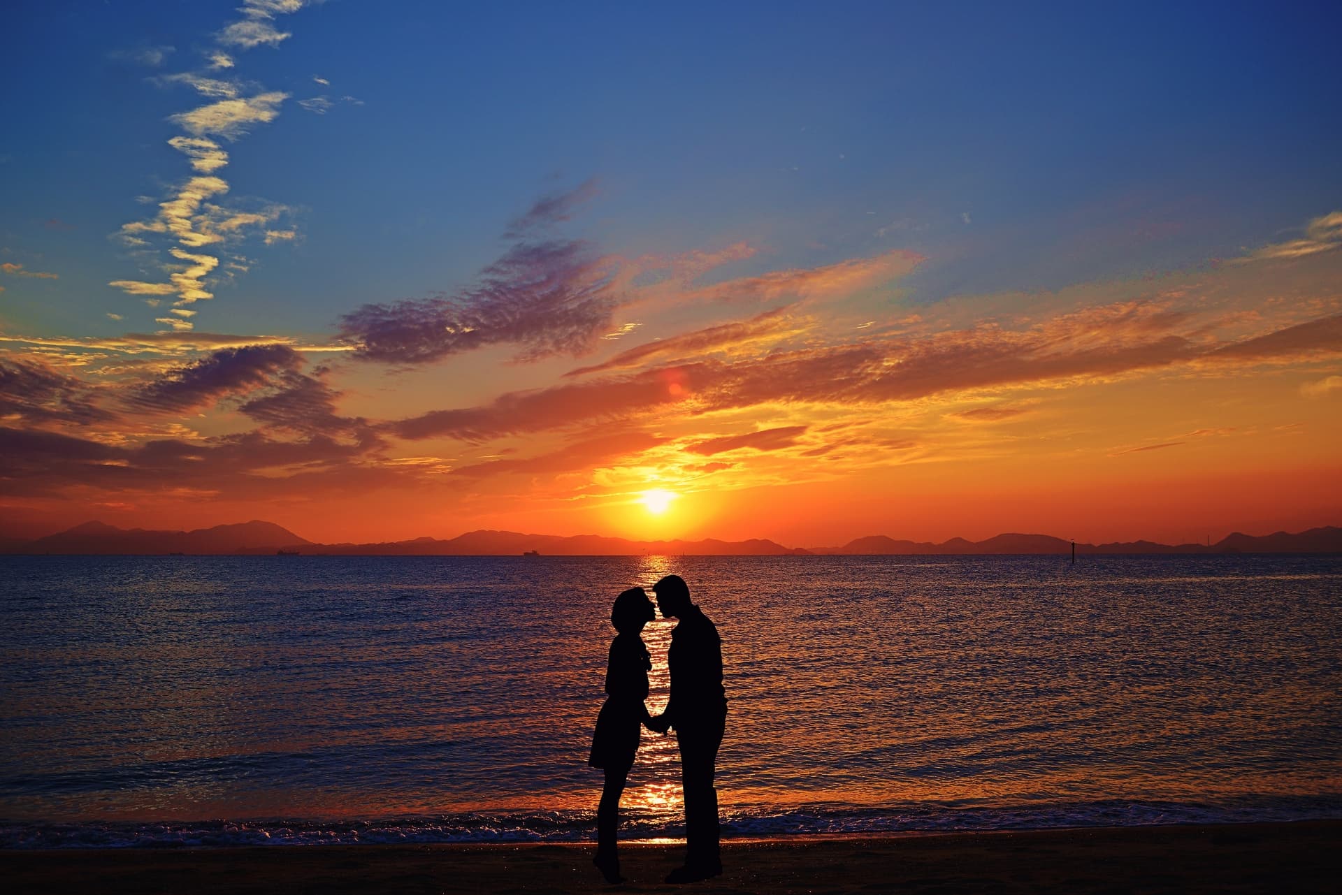 覚醒したツインレイ男性と夕日の海辺で見つめ合っている女性の画像